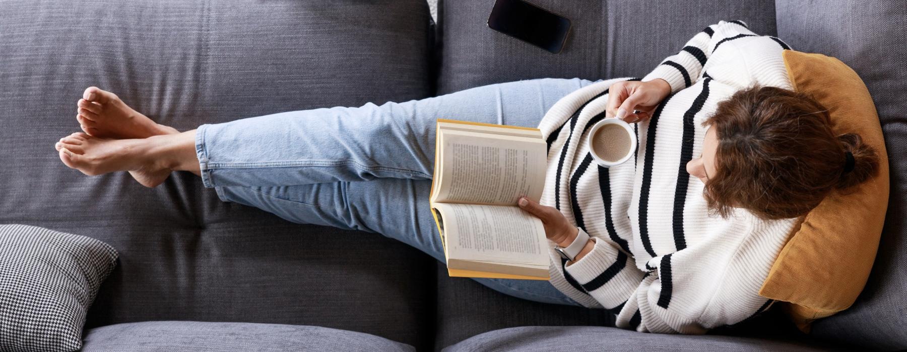 a person lying on a couch reading a book