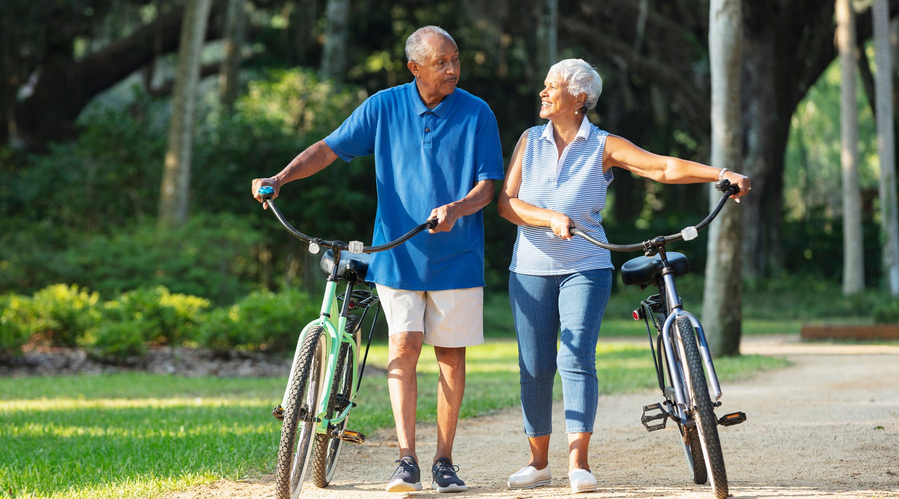 a couple walking bikes under the trees
