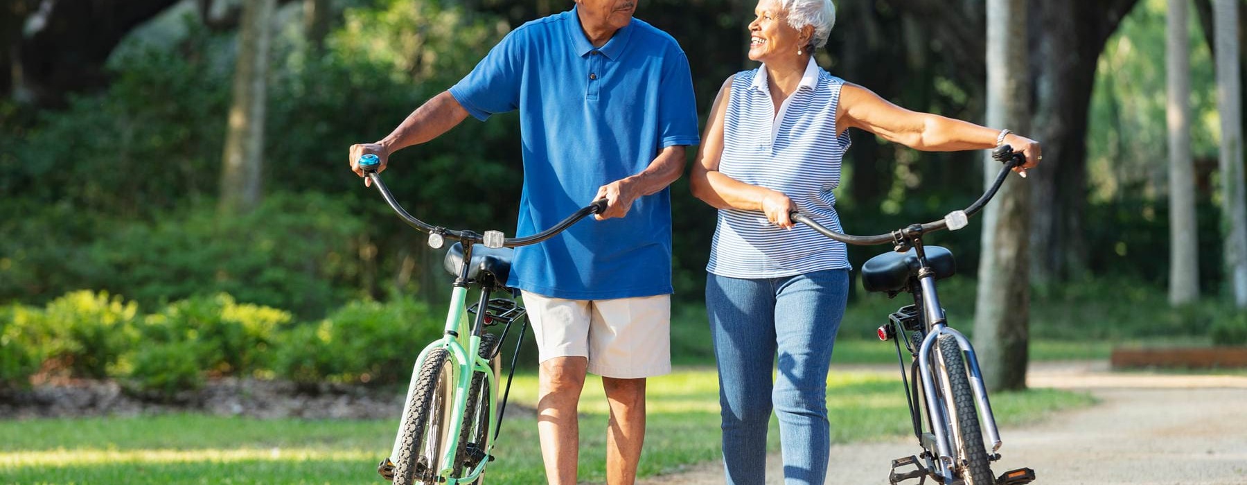 a couple walking bikes under the trees